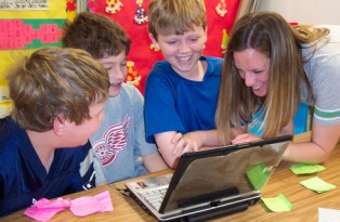 teacher working with three students by a laptop 