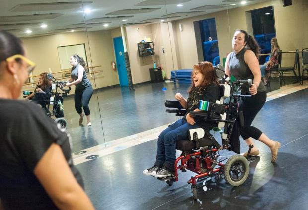 Jolly woman dancing around with a joyful student in a wheelchair.